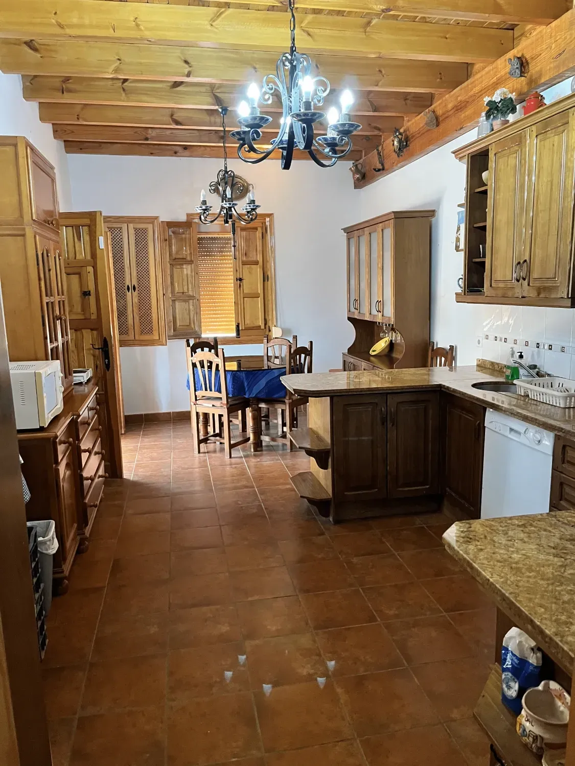 Cocina con gabinetes de madera, piso de baldosas rústicas y lámpara de araña.