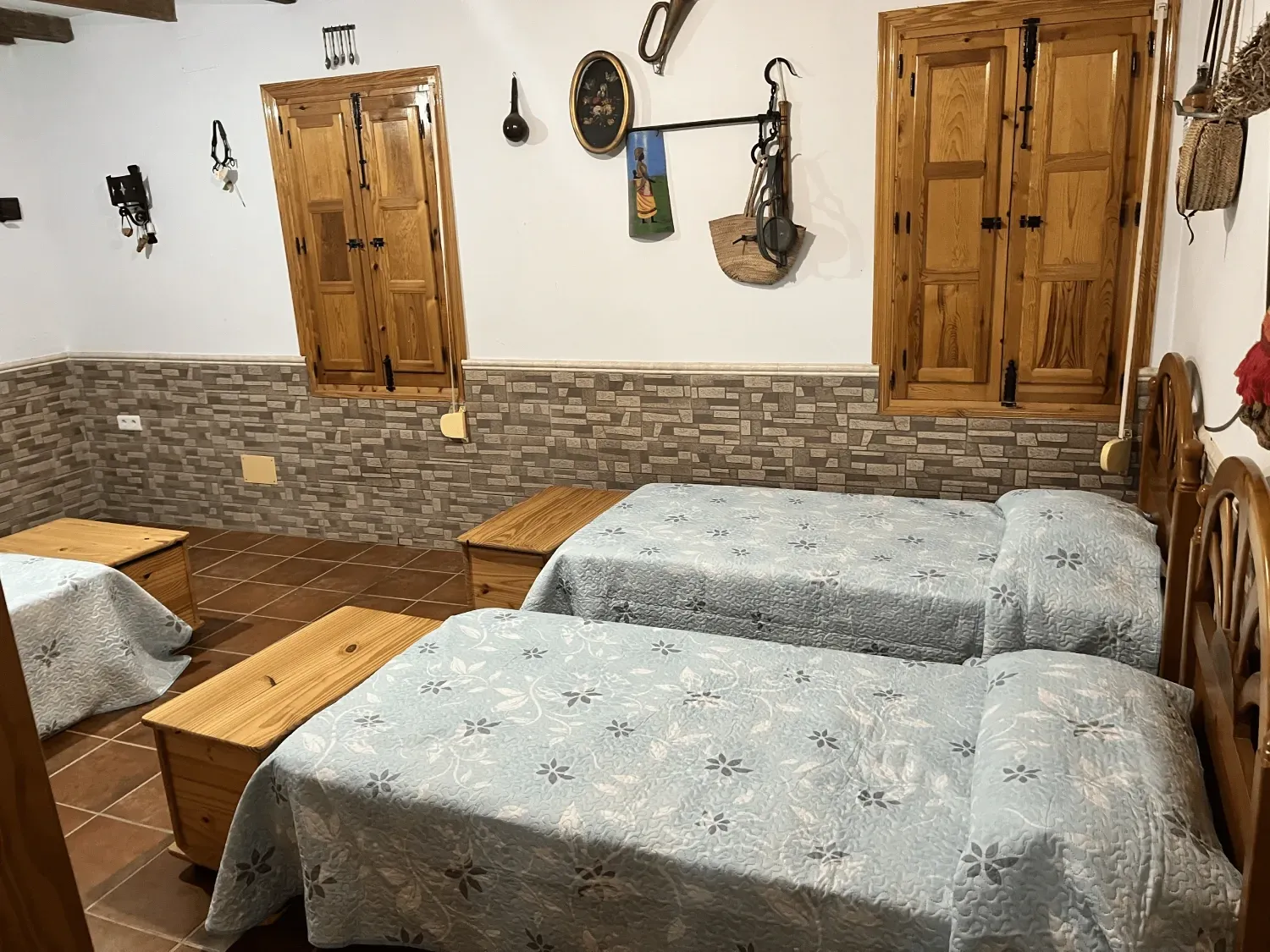 Dormitorio con dos camas individuales, mesitas de noche de madera, ventanas con contraventanas y decoración rústica.