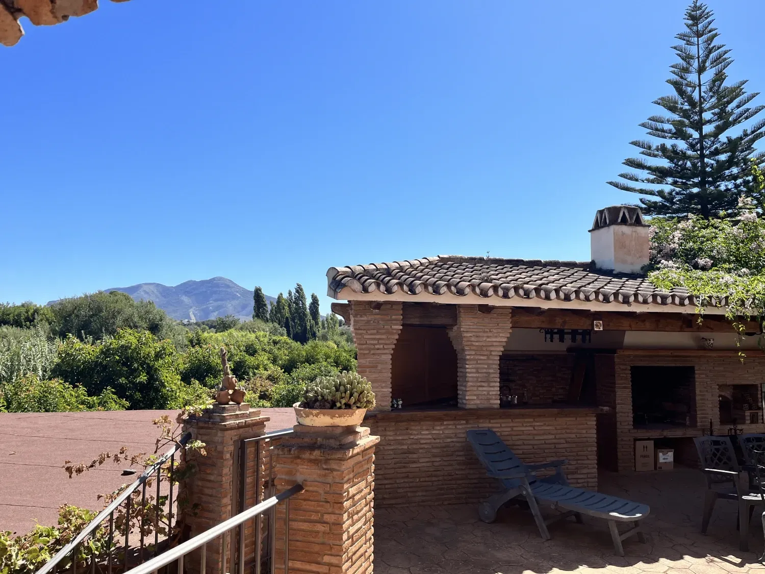 Patio exterior soleado con estructura de ladrillo, vista a la montaña y tumbona.