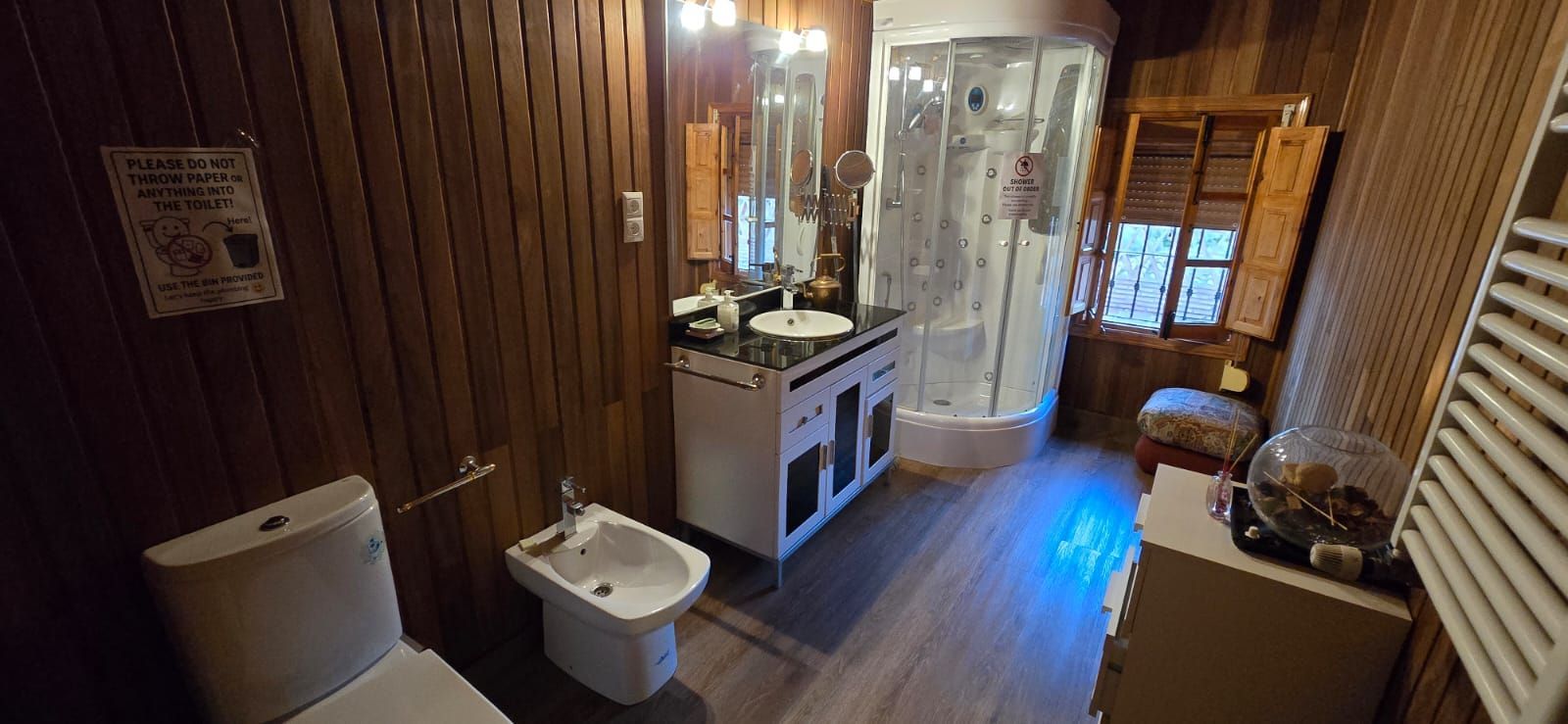 Baño con paneles de madera, ducha, inodoro, lavabo y bidet.