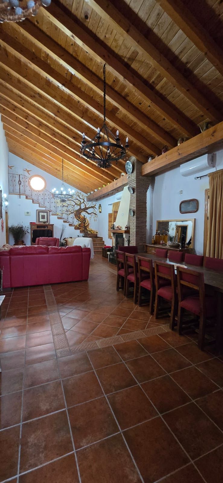 Interior de una casa espaciosa con techos altos de madera, pisos de baldosas rojas y una gran mesa de comedor.