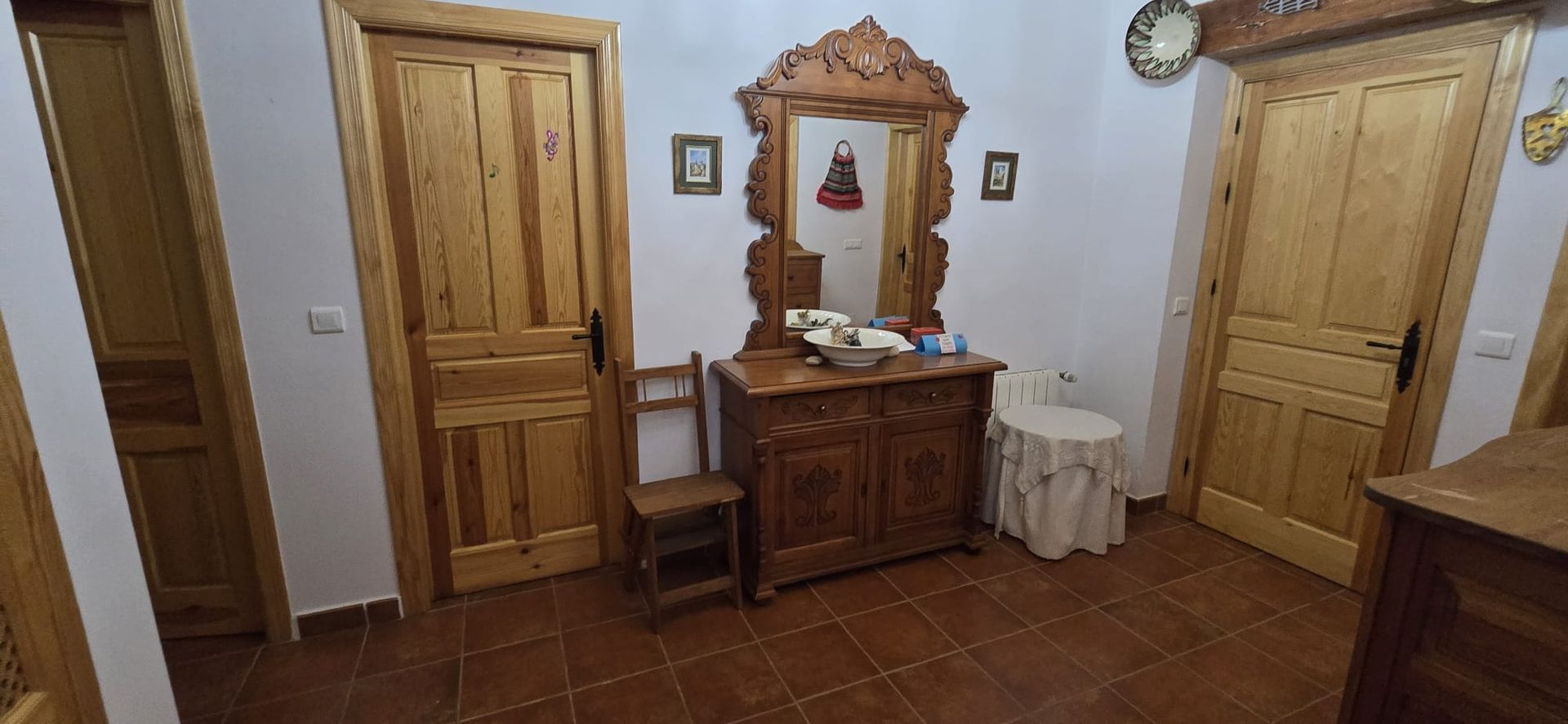 Pasillo con puertas de madera, espejo y una silla pequeña. Suelo de baldosas.