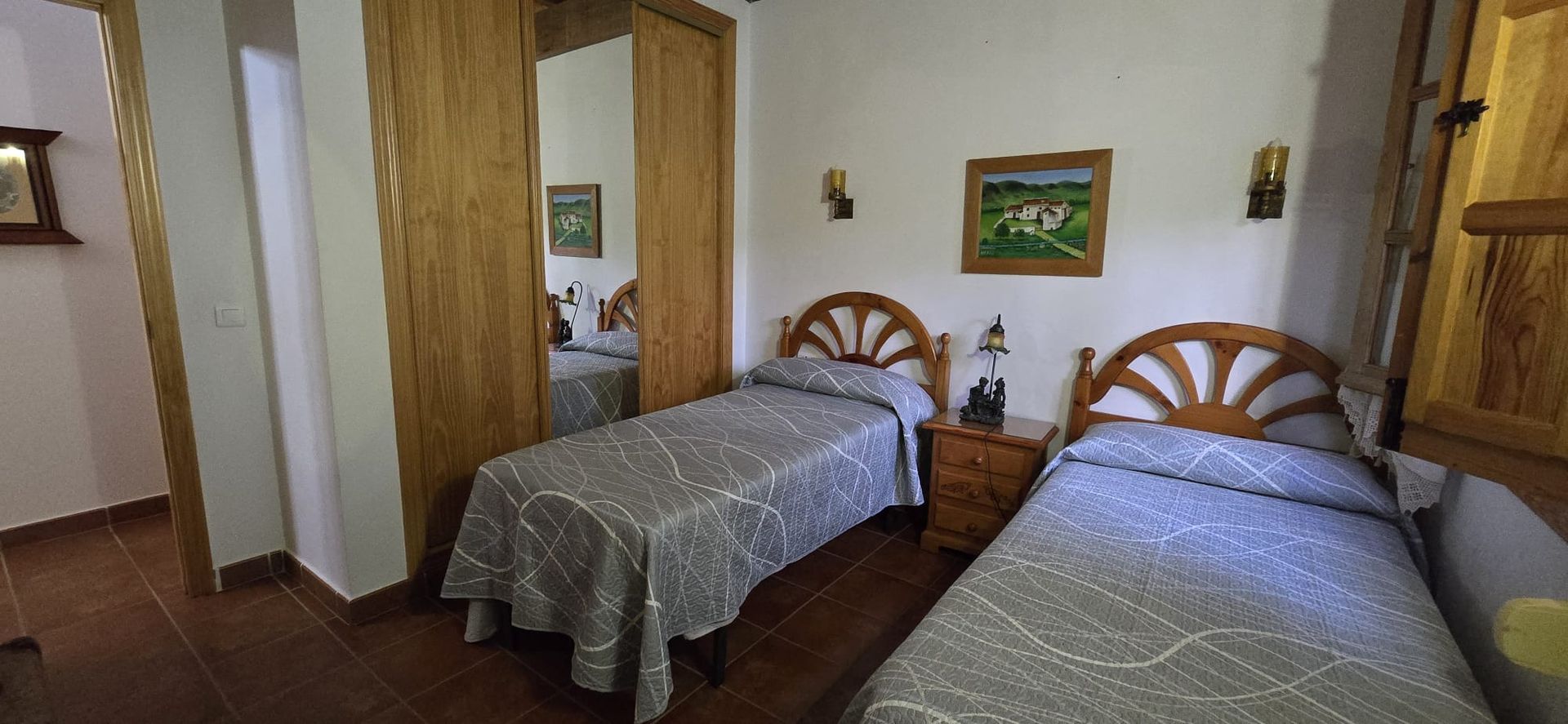 Dos camas individuales en un dormitorio con cabeceros de madera, mesita de noche y armario con espejo.