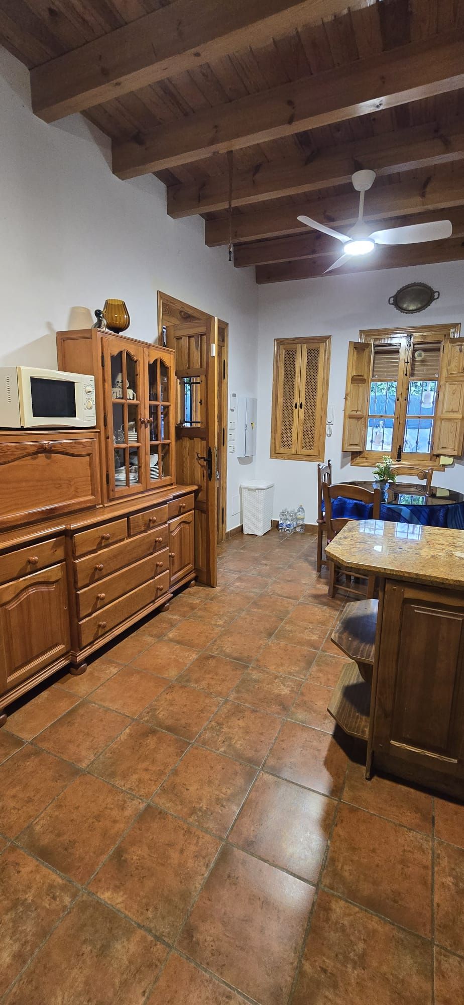 Cocina con gabinetes de madera, piso de baldosas de terracota, vigas de madera en el techo y ventanas.