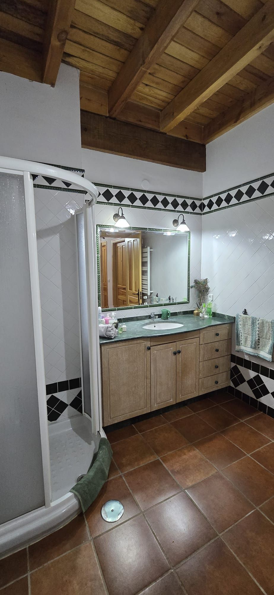 Baño con techo de madera, tocador, cabina de ducha y piso de baldosas.