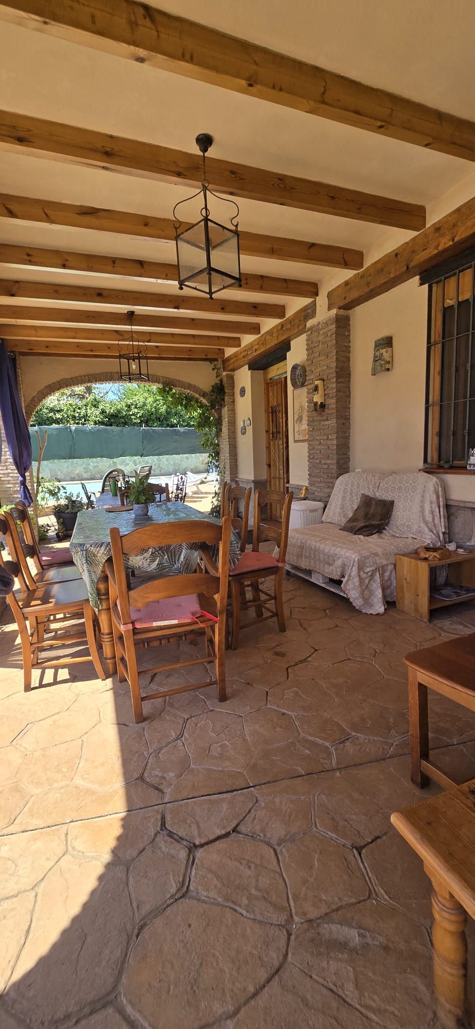 Patio cubierto con asientos y mesa, con vista al área al aire libre.