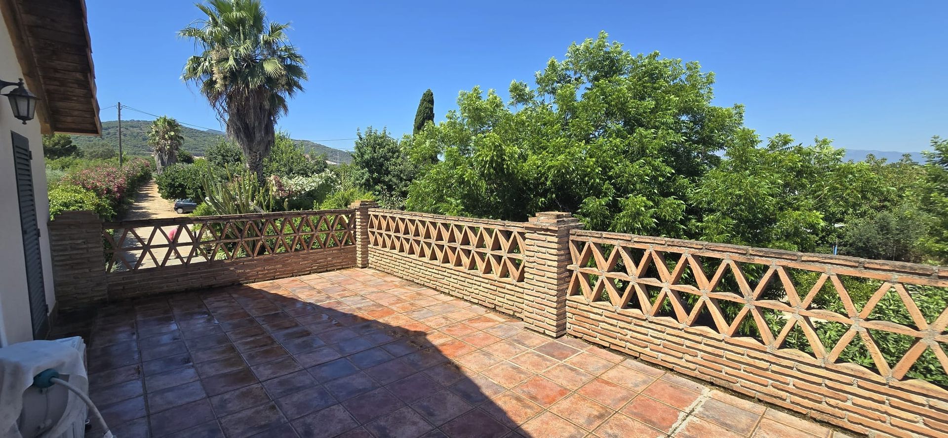 Patio de ladrillo con barandilla con diseño triangular con vista a frondosos árboles y un cielo azul claro.