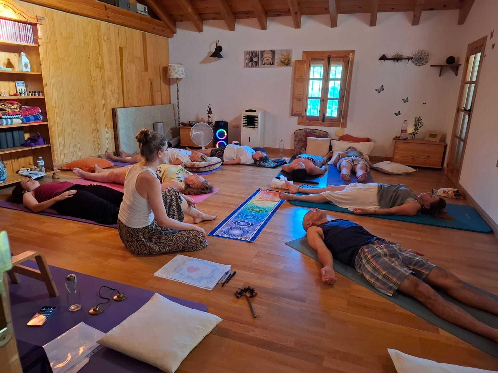 Un grupo de personas practicando yoga en una sala soleada. Una mujer dirige la clase.