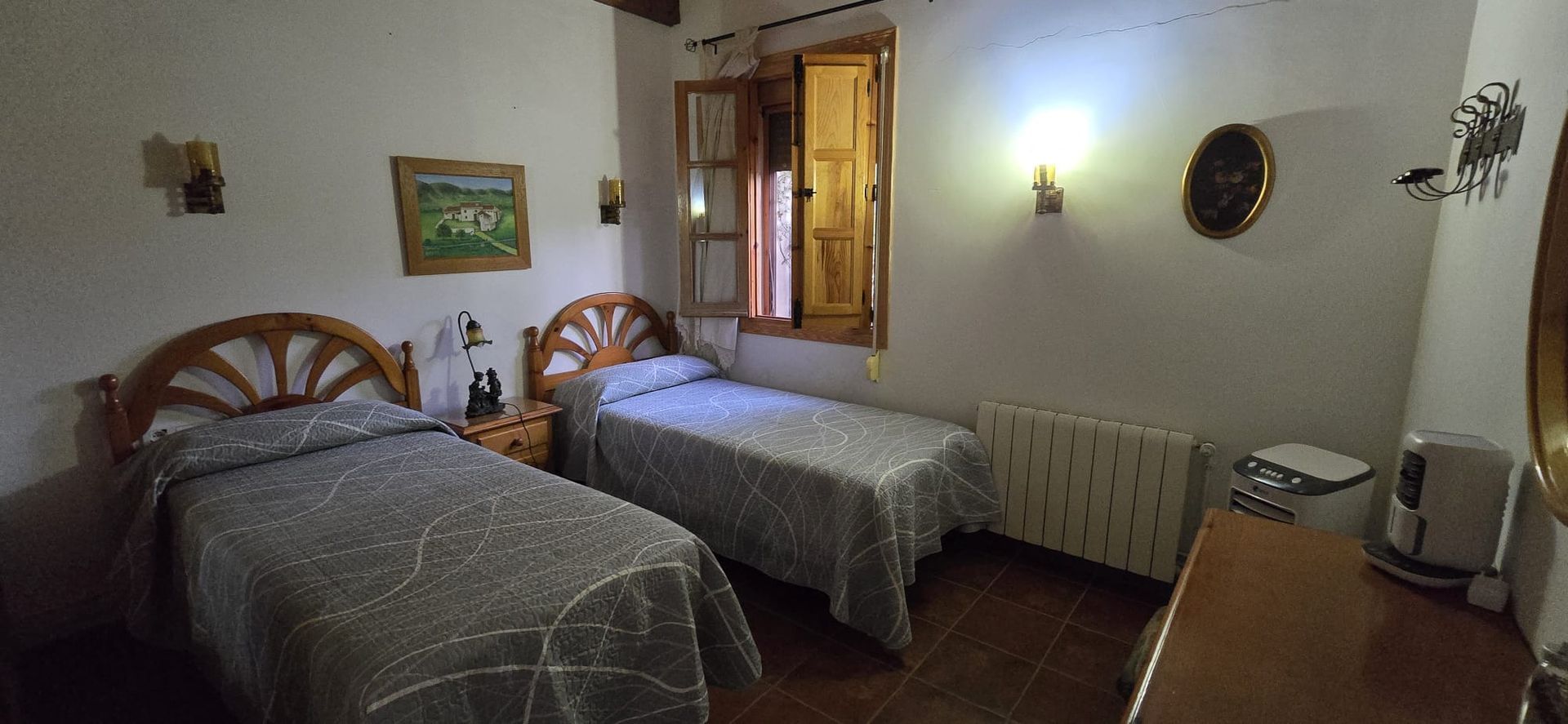 Dormitorio con dos camas individuales, ventana y cómoda. Las camas tienen cabeceros de madera y colchas grises.