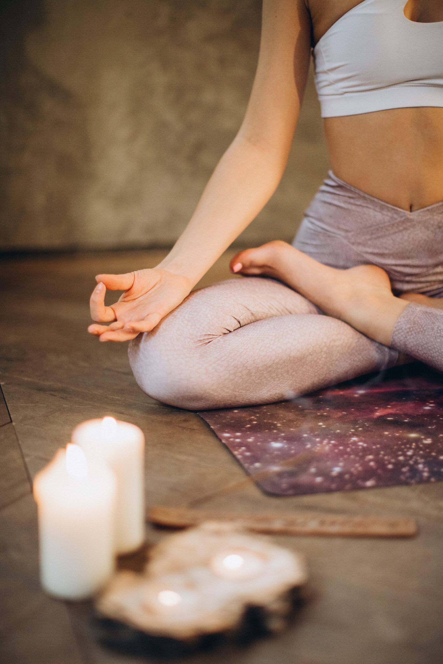 Mujer en pose de yoga, meditando con las manos en mudra; velas en el suelo.