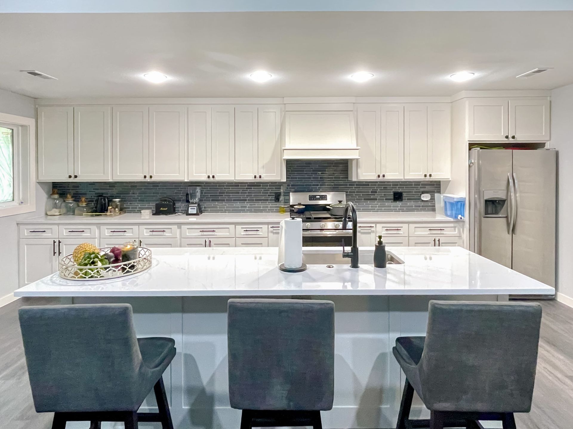 Modern kitchen with white cabinets, island, and gray bar stools. Stainless steel fridge.