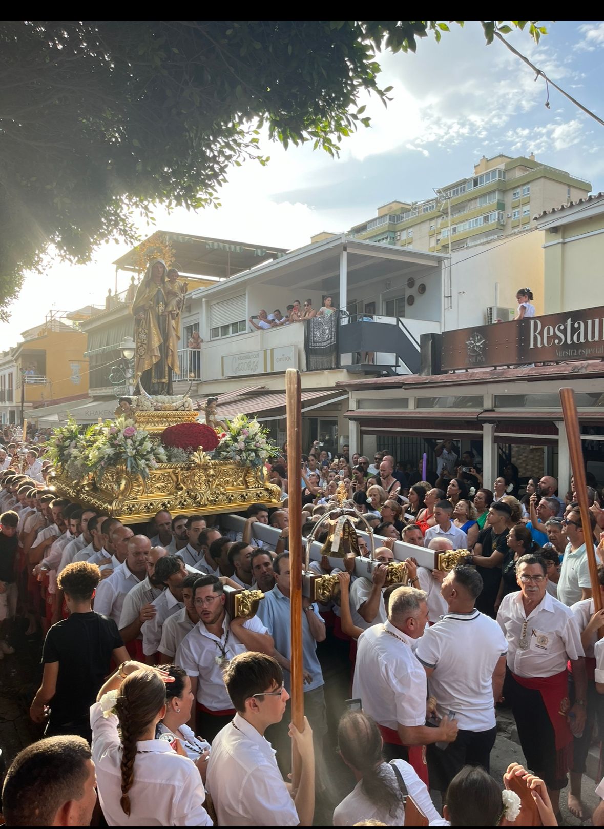 Personas portando una carroza decorada en una multitudinaria procesión callejera.