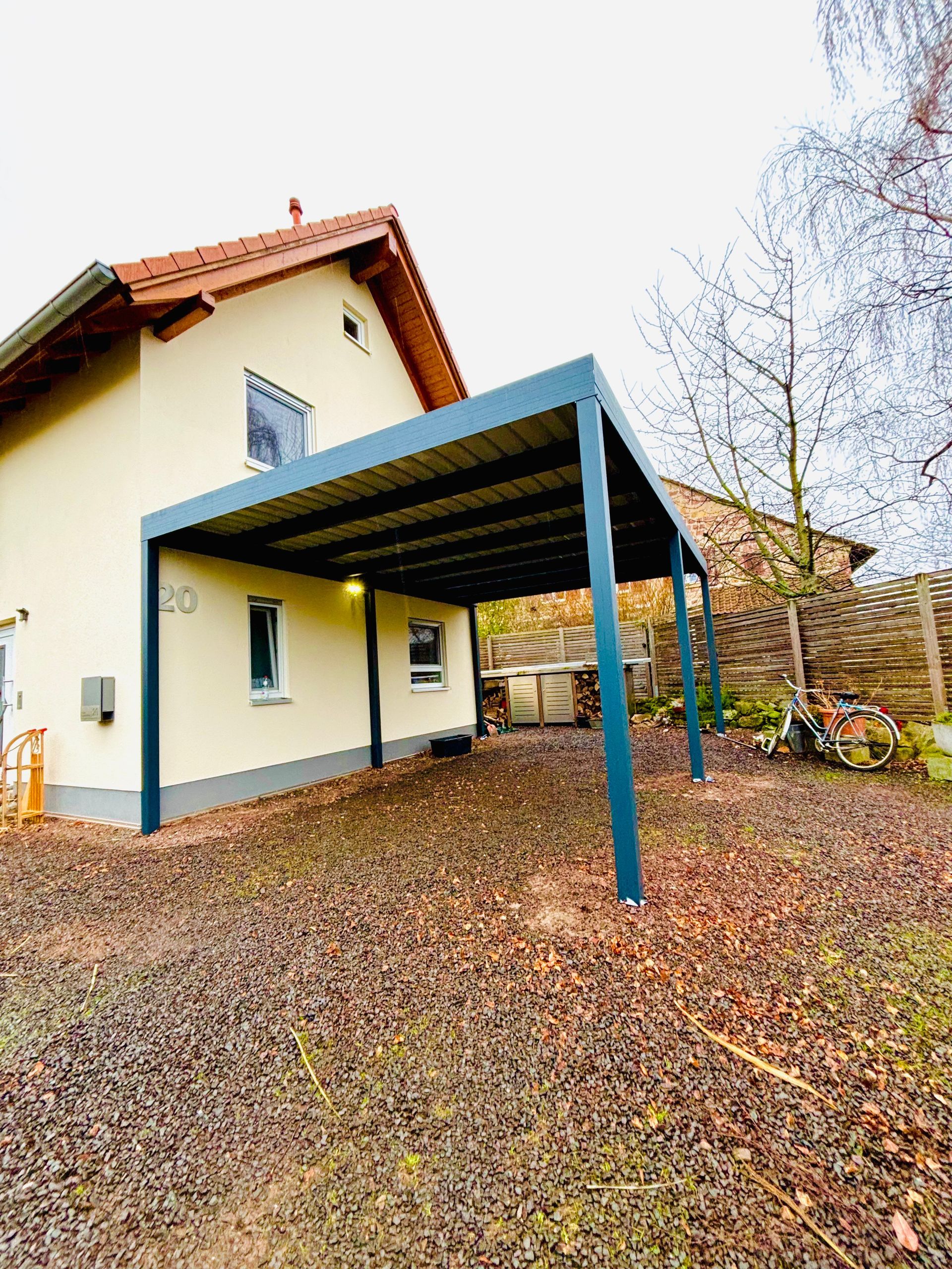 Ein Carport mit Wänden aus Holzlatten, einem transparenten Dach und einem auf einer gepflasterten Auffahrt geparkten Lieferwagen.
