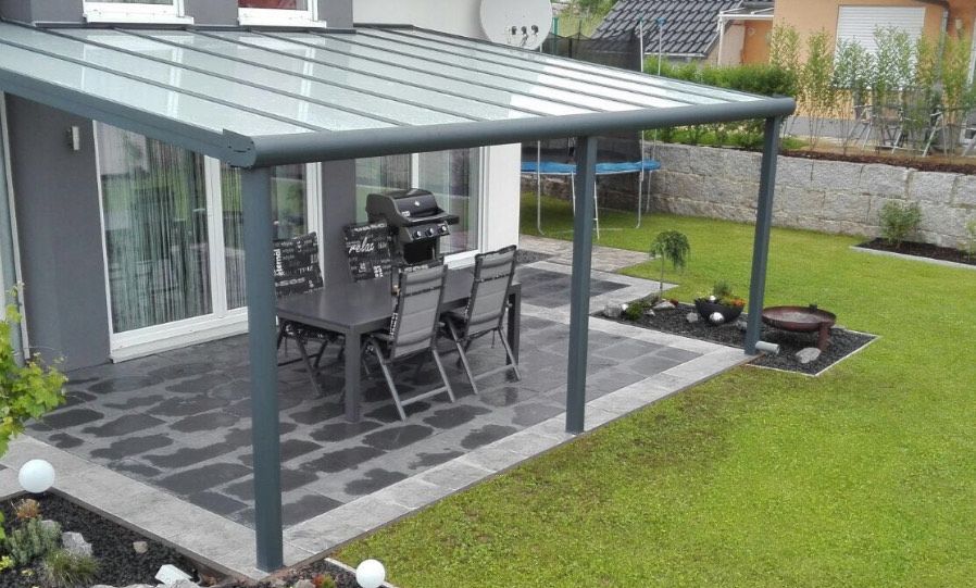 Ein Carport mit Wänden aus Holzlatten, einem transparenten Dach und einem auf einer gepflasterten Auffahrt geparkten Lieferwagen.