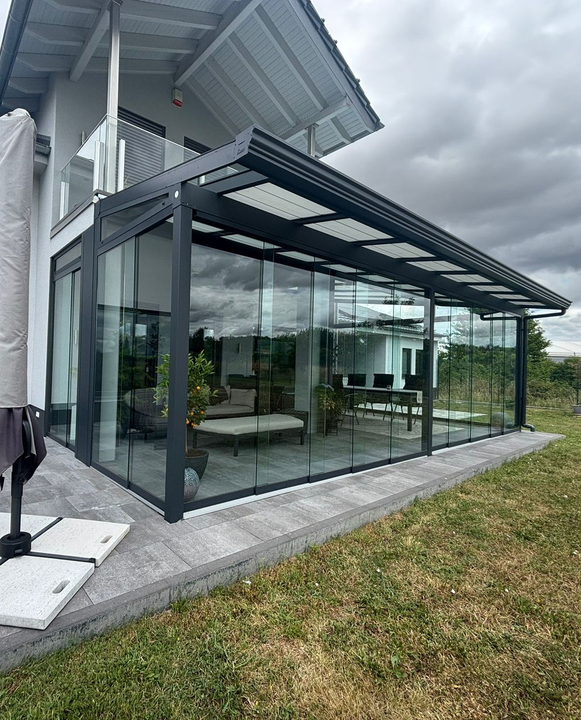 Moderne Terrassenüberdachung aus Aluminium und Glas an Einfamilienhaus mit bodentiefen Schiebeelementen
