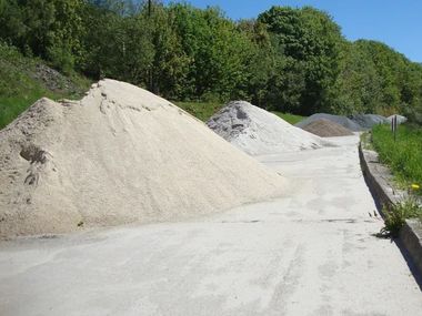 Kieshaufen entlang einer asphaltierten Straße neben dichtem Grün und Sträuchern