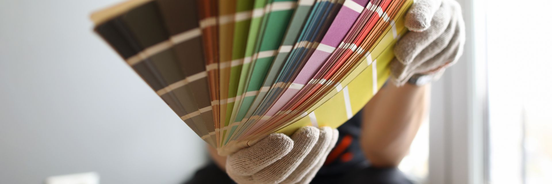 Des mains gantées tiennent un nuancier de peinture étalé en éventail