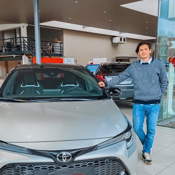 Un homme se tient à côté d'une Toyota GR Corolla argentée dans une concession automobile.