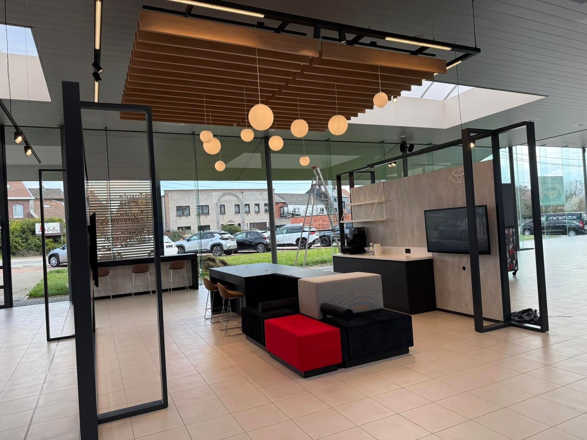 Intérieur de bureau moderne avec sièges, écrans d'affichage et suspensions lumineuses rondes, avec une vue sur la rue en arrière-plan.