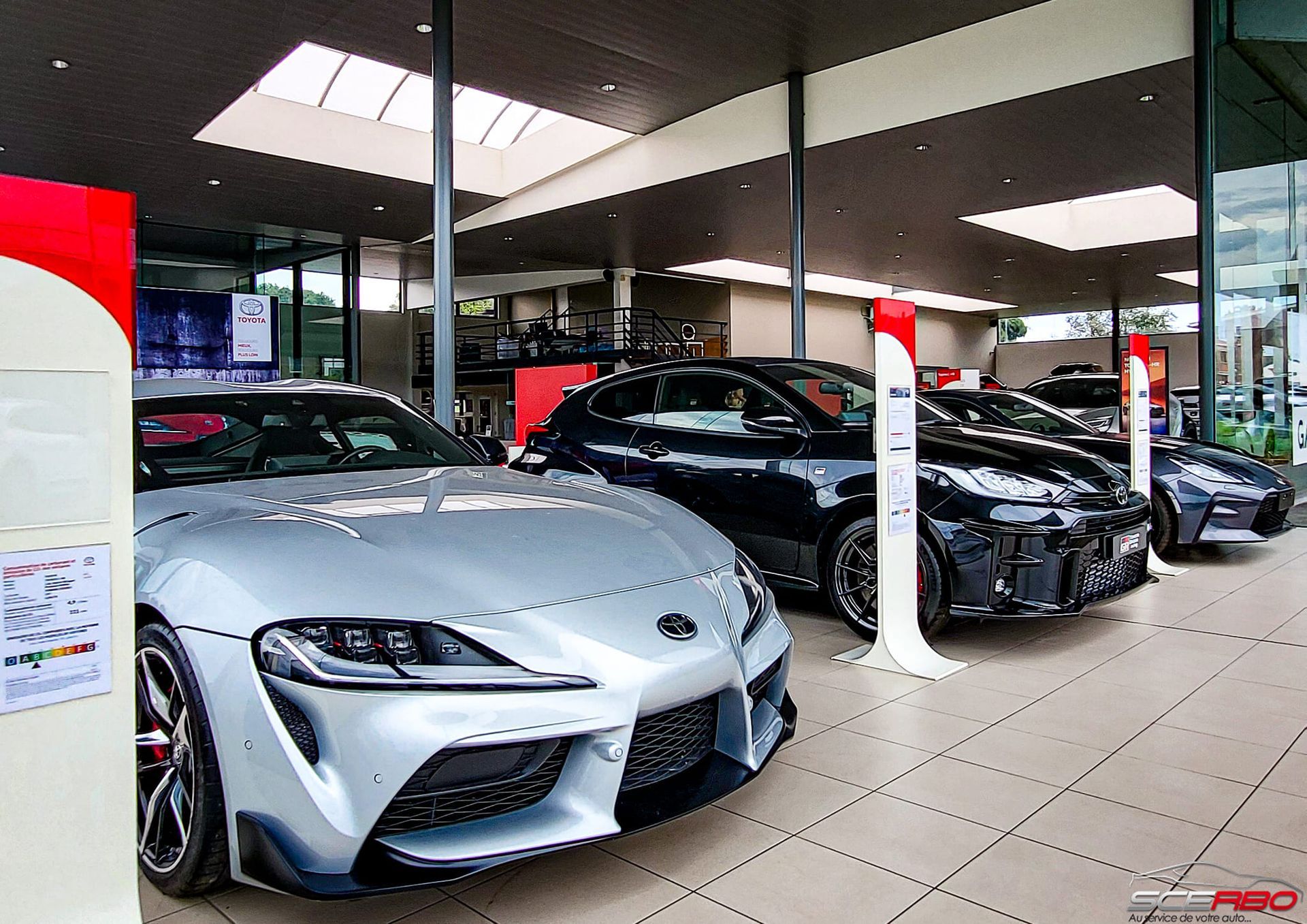 Une Toyota Supra argentée et d'autres voitures noires sont exposées dans la salle d'exposition d'un concessionnaire automobile.