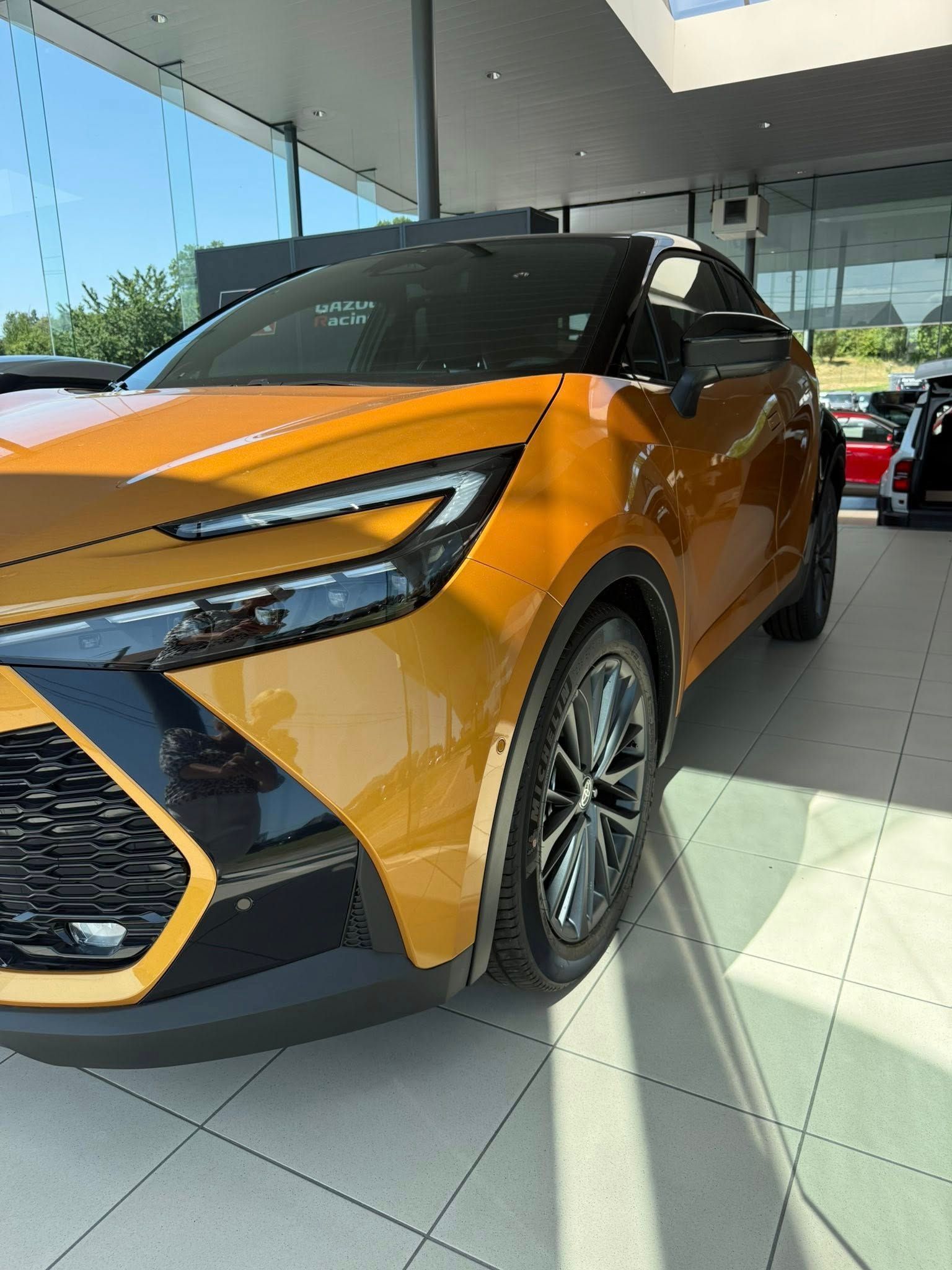 Un SUV Toyota jaune doré est garé à l'intérieur d'un showroom de concessionnaire aux parois vitrées.