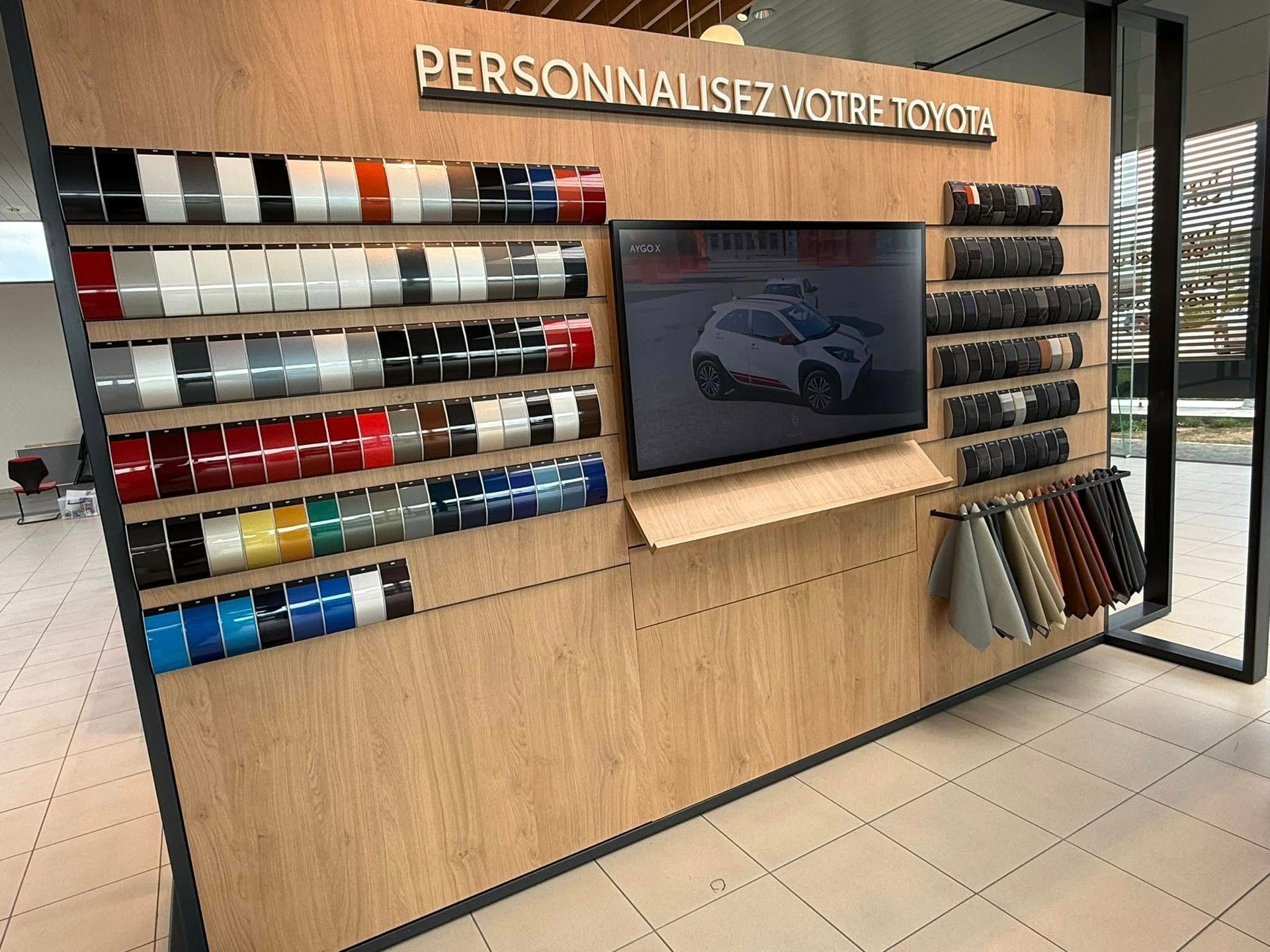 Présentoir mettant en valeur les options de personnalisation des voitures Toyota : couleurs de peinture, échantillons de tissus et un écran.