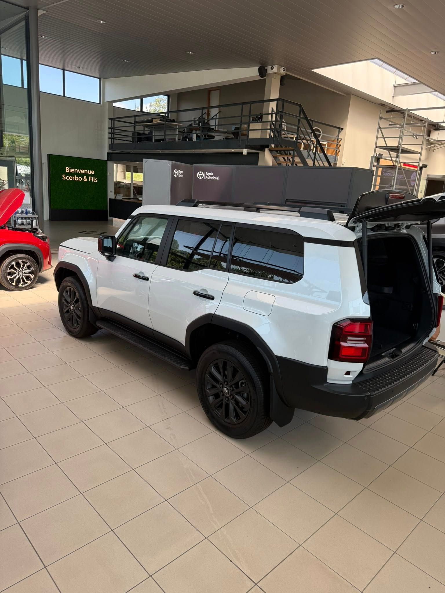 Un SUV Ford Bronco blanc, avec l'arrière ouvert, est stationné à l'intérieur du hall d'exposition d'un concessionnaire.