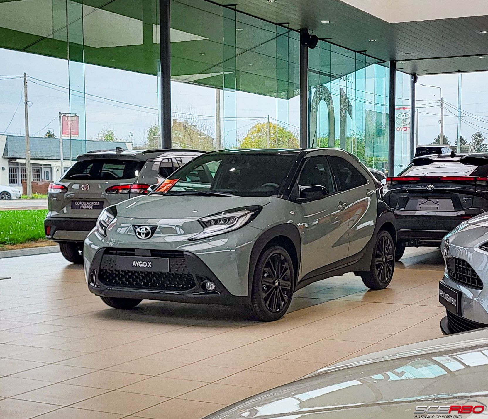 Toyota Aygo X dans un showroom, grise avec des accents noirs, entourée d'autres véhicules.