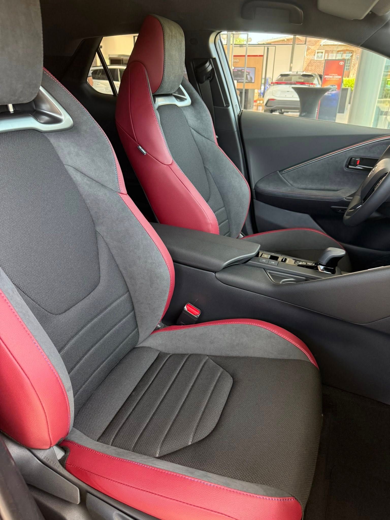 Intérieur de voiture noir et rouge avec sièges, accoudoir et volant.