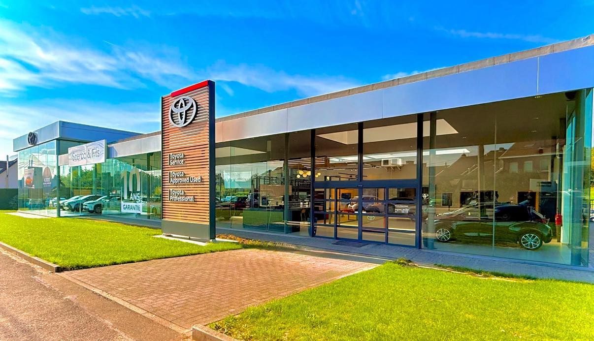 Concessionnaire Toyota avec façade vitrée, pelouse verte et ciel bleu.