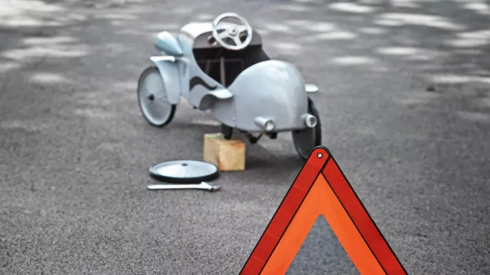 Voiture miniature calée sur un bloc avec roue de secours et panneau de danger routier sur l'asphalte.