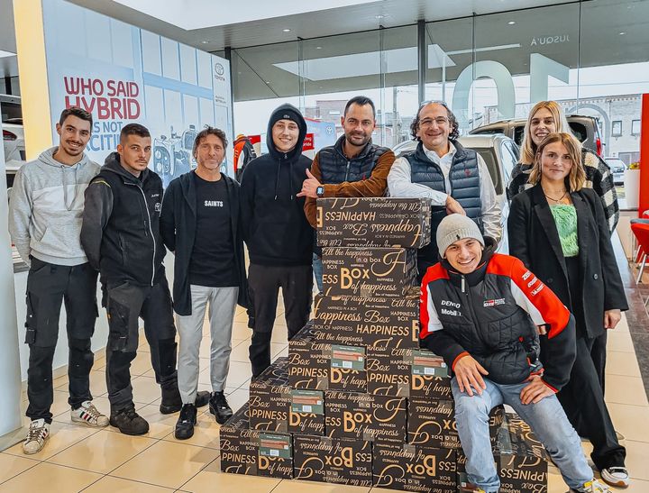 Groupe de personnes posant avec une grande pile de cartons à l'intérieur d'une salle d'exposition.