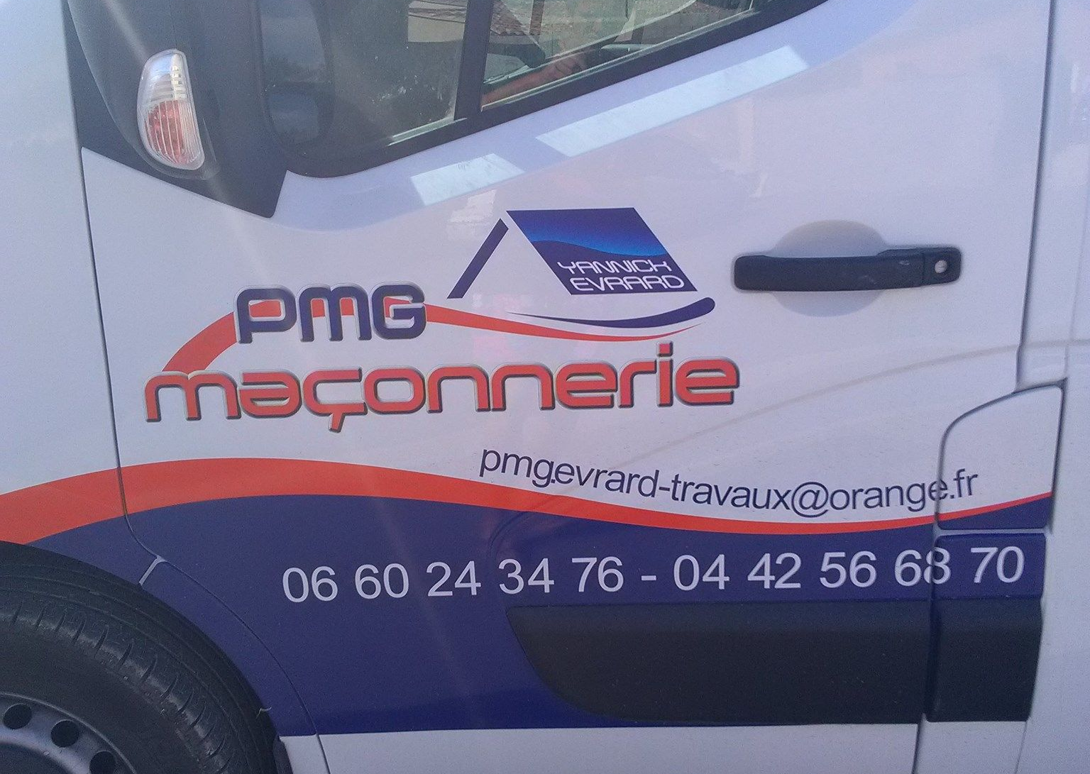 Camionnette blanche avec logo PMG Maçonnerie, numéros de téléphone et adresse e-mail en orange, rouge et bleu.