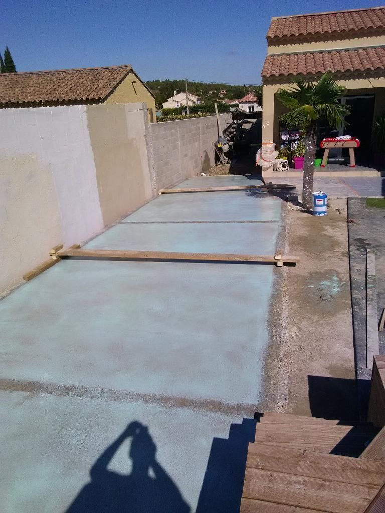 Patio en béton en construction à l'extérieur avec l'ombre d'une personne tenant un téléphone.