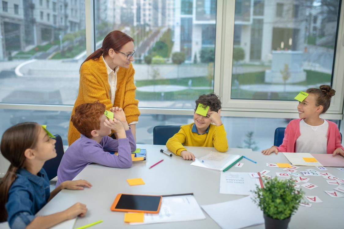 Un grupo de niños está sentado en una mesa con notas adhesivas en sus caras.