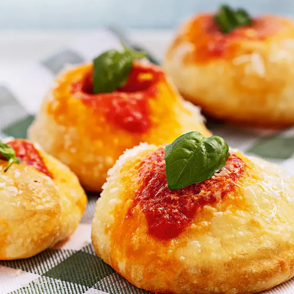 Gros plan sur une pizza garnie de feuilles de basilic, de mozzarella et de sauce tomate, servie sur une assiette en pierre.