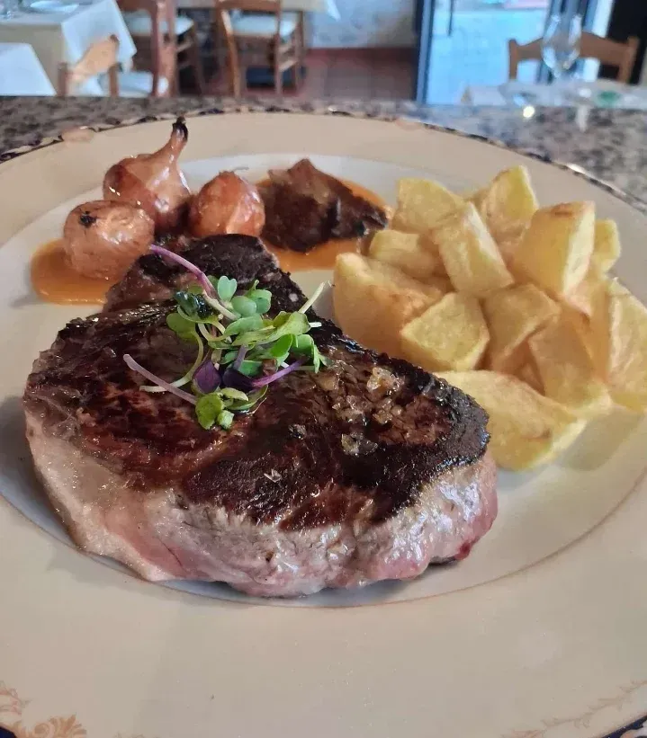 Bistec a la parrilla con patatas y salsa en un plato blanco.
