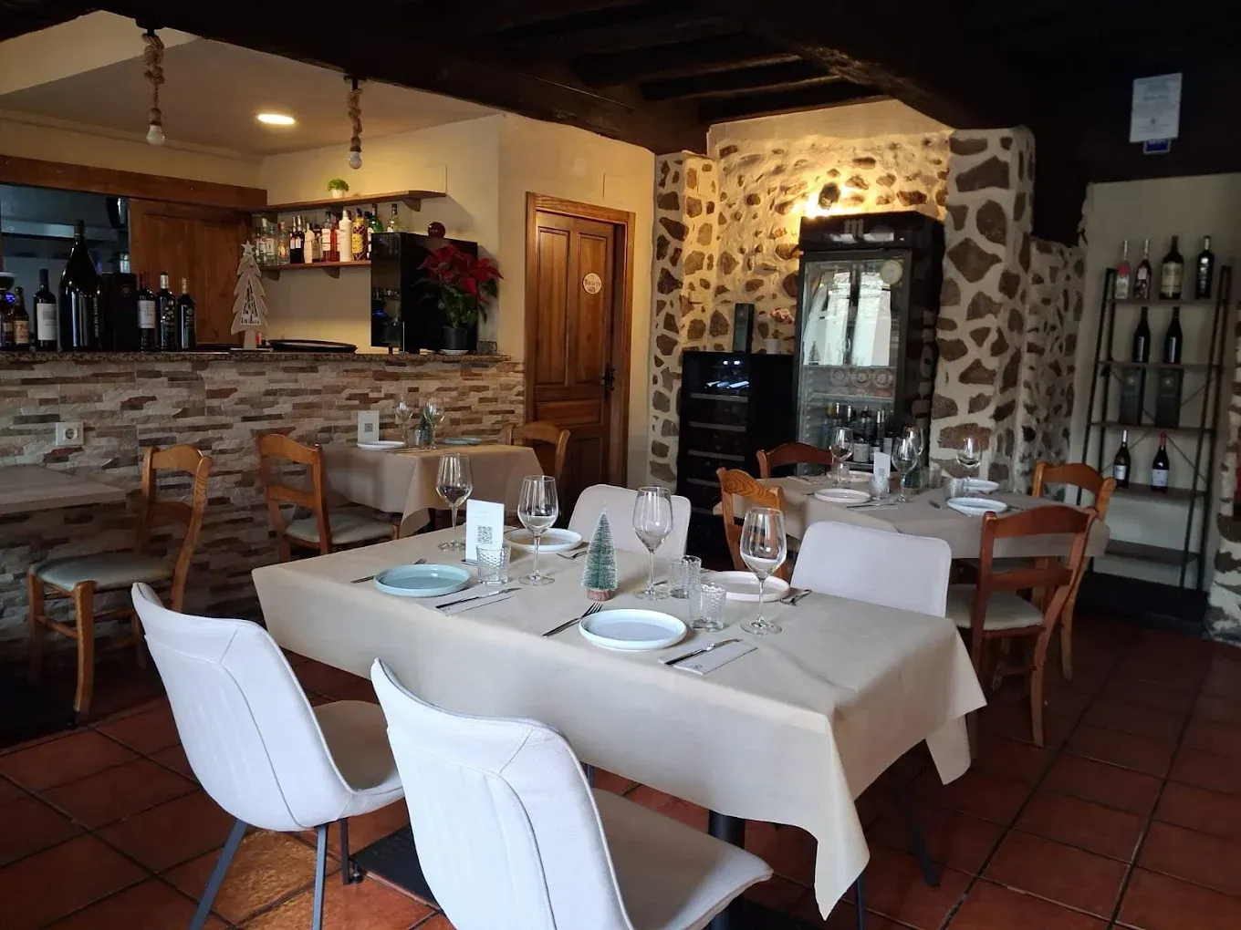 Interior de restaurante con mesas preparadas para comer, paredes de piedra y un botellero.