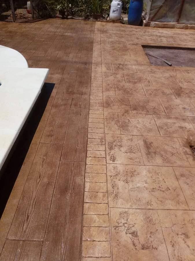 Un patio de hormigón con borde de madera junto a una piscina.