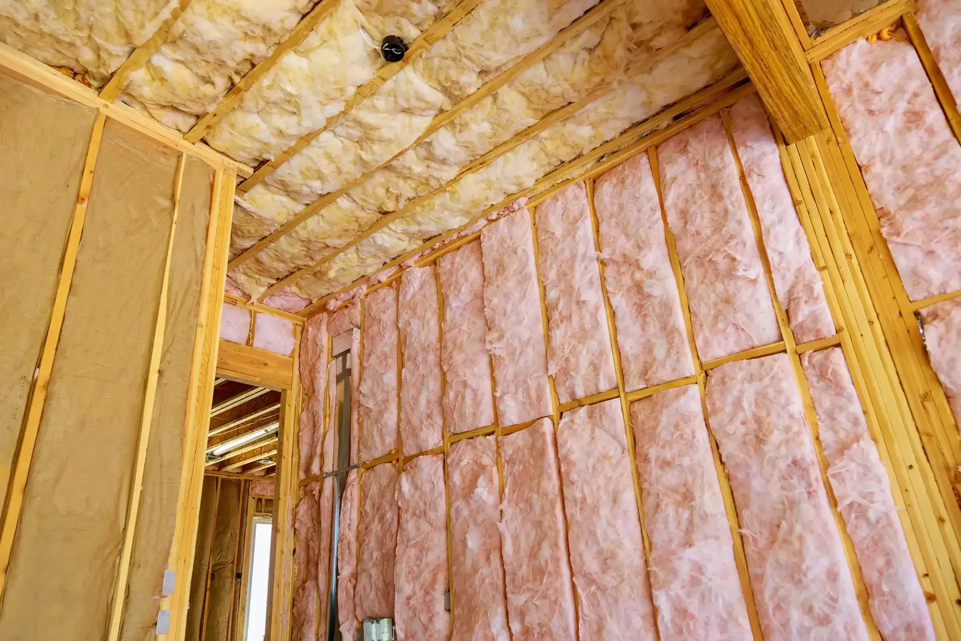 Unfertige Innenwand- und Deckenkonstruktion in einem Holzgebäude, die mit rosa Glasfaser-Dämmmatten gefüllt ist.