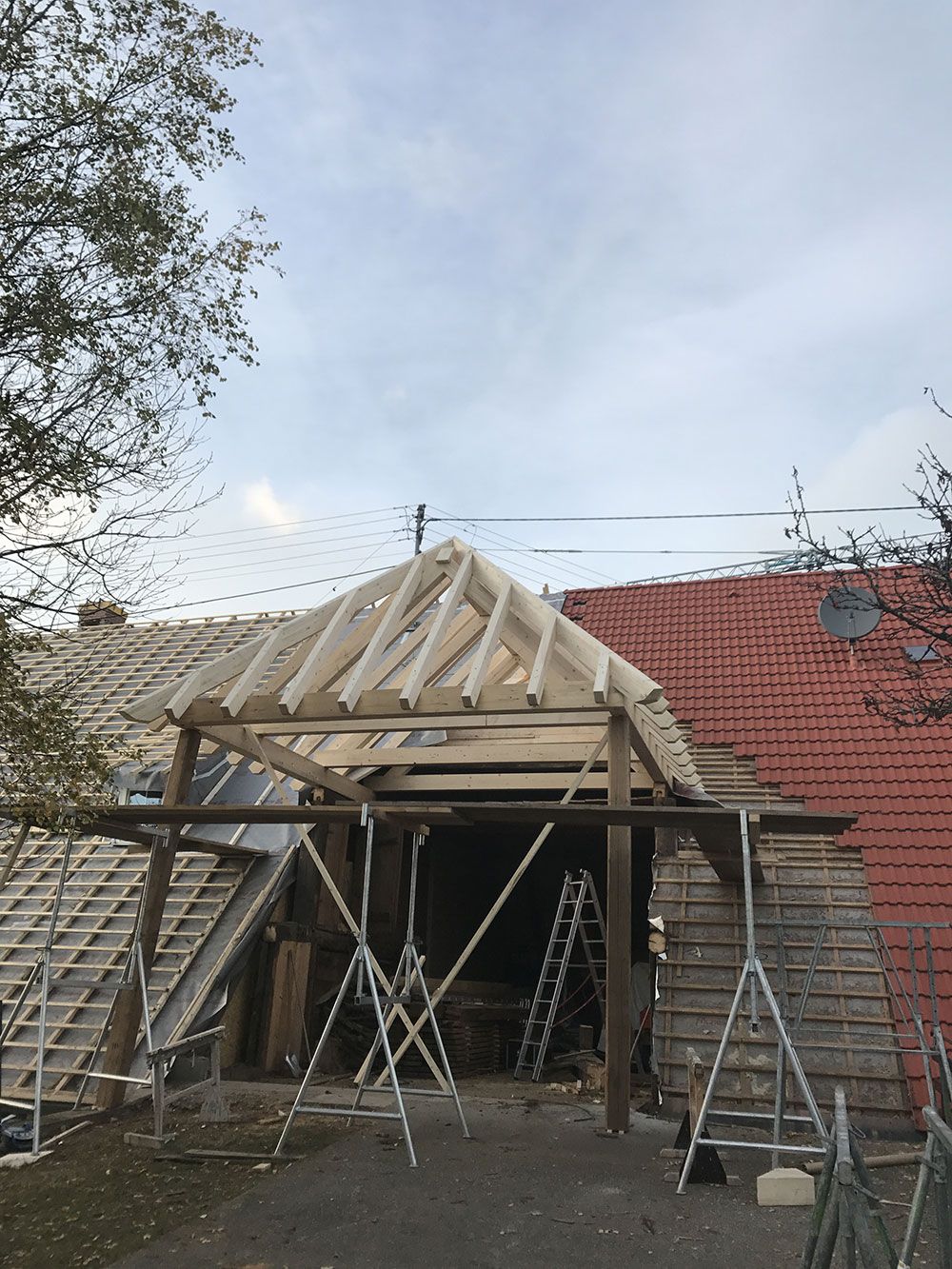 Ein im Bau befindliches Haus, das ein freiliegendes hölzernes Dachgerüst und ein Baugerüst zeigt, mit einer roten Backsteinmauer auf der rechten Seite.