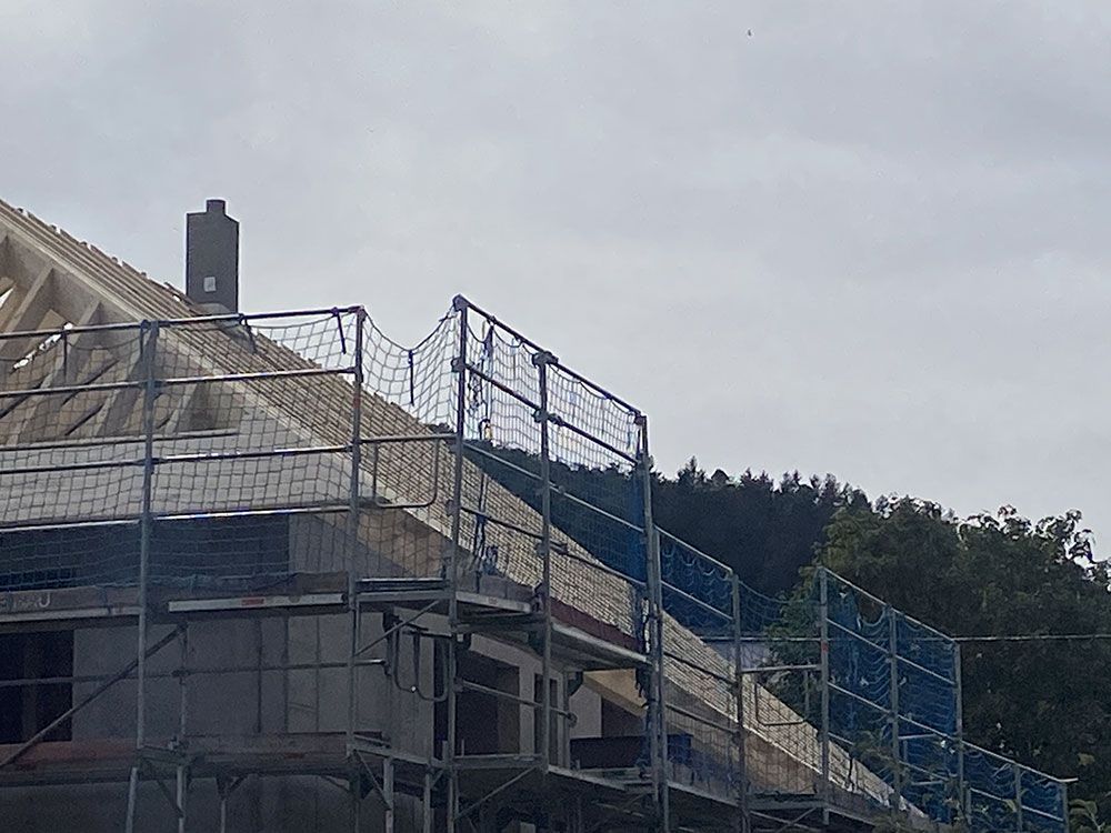 Ein teilweise errichtetes Hausdach mit hölzernen Dachsparren und umlaufendem Gerüst unter bewölktem Himmel.