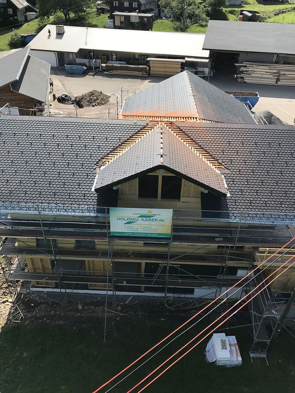 Eine Luftaufnahme eines im Bau befindlichen Gebäudes mit einem markanten Giebeldachgaubenfenster und einem Gerüst an einem Holzdach.