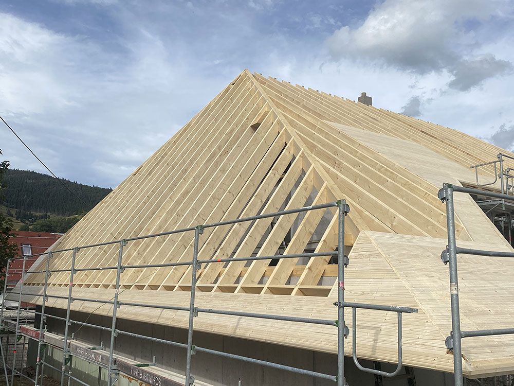 Ein im Bau befindliches Haus, das das Holzgerüst und das teilweise mit Dachplatten versehene Dach zeigt, gesehen von hinter einem Baugerüst.
