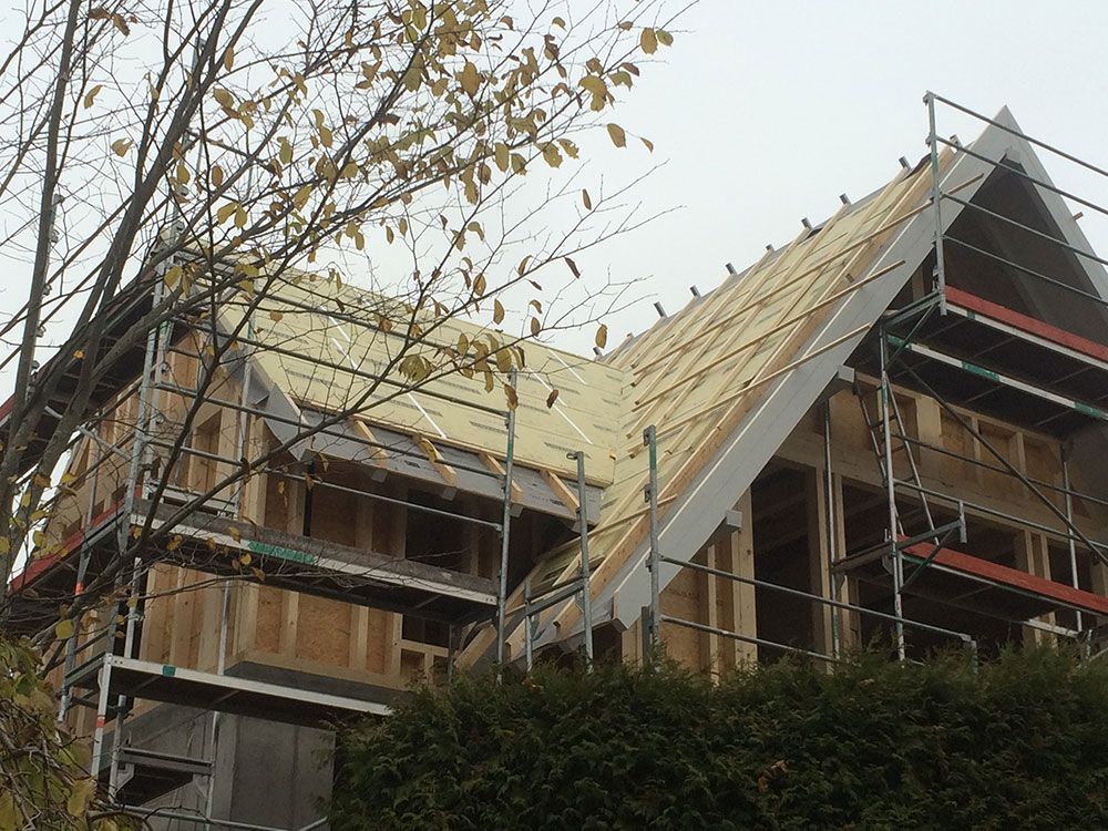 Ein im Bau befindliches Haus mit Holzrahmen und freiliegenden Dachsparren, umgeben von einem Metallgerüst.