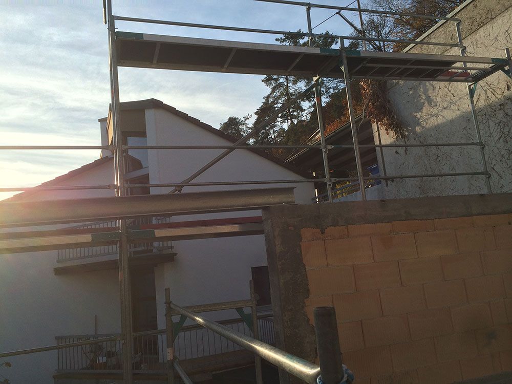 Bei Sonnenuntergang steht vor einem weißen Haus mit braunem Ziegeldach ein Metallgerüst.