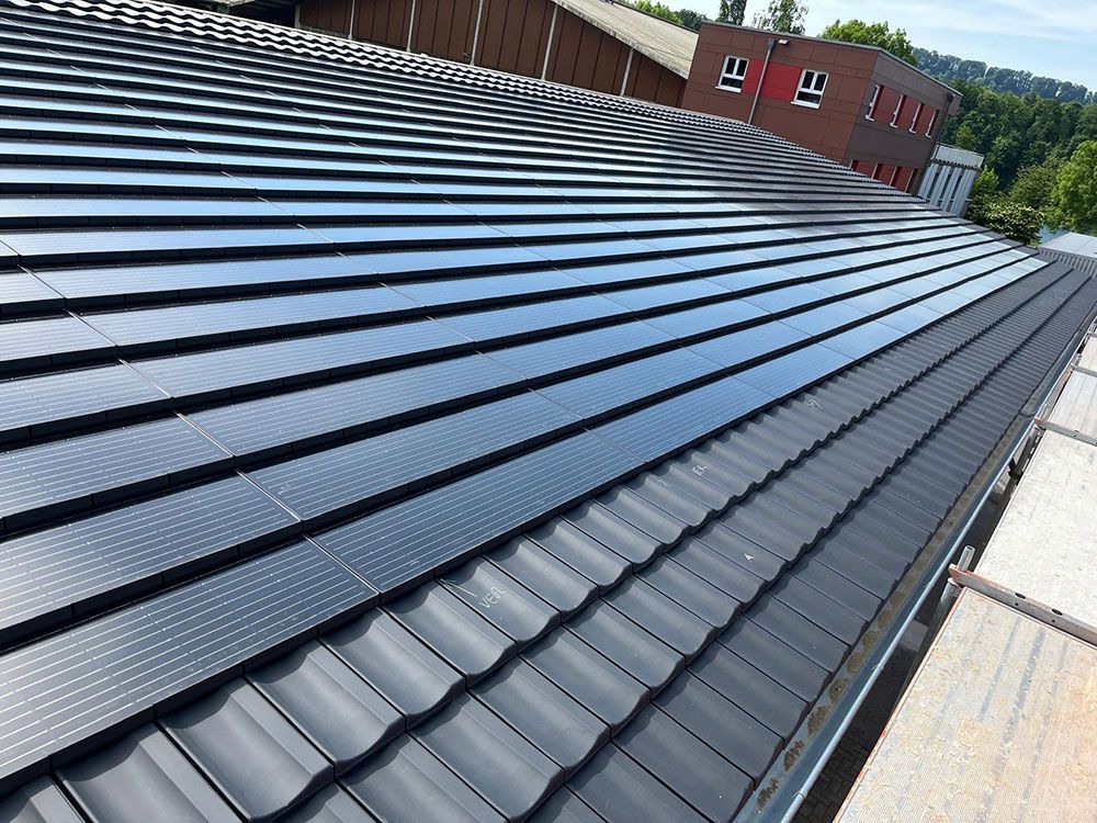 Ein geneigtes Dach mit Reihen integrierter Solarpaneele über Abschnitten aus dunklen, gebogenen Dachziegeln.