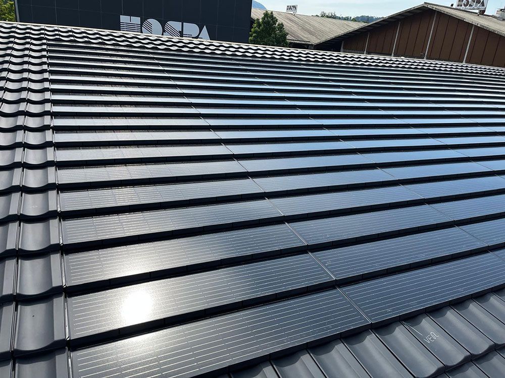 Ein geneigtes Dach mit integrierten Solardachziegeln, die sich harmonisch in das Gesamtbild der herkömmlichen dunklen Dachziegel einfügen.