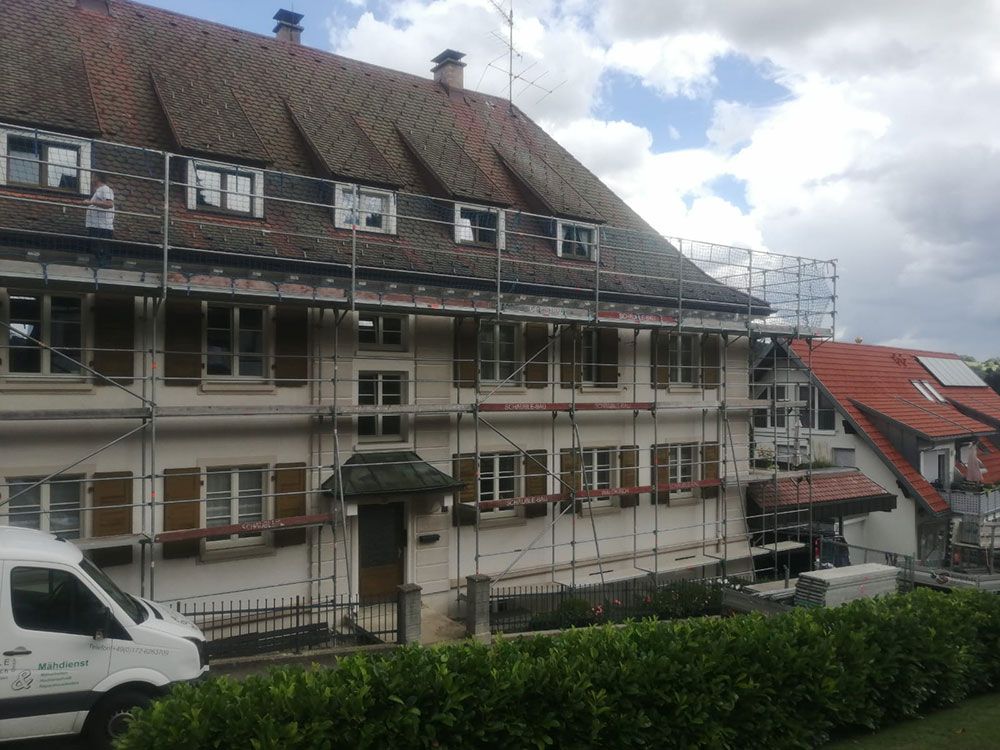 Ein mehrstöckiges Haus, das wegen Renovierungsarbeiten mit einem Gerüst versehen ist; im Vordergrund ist ein weißer Lieferwagen geparkt.