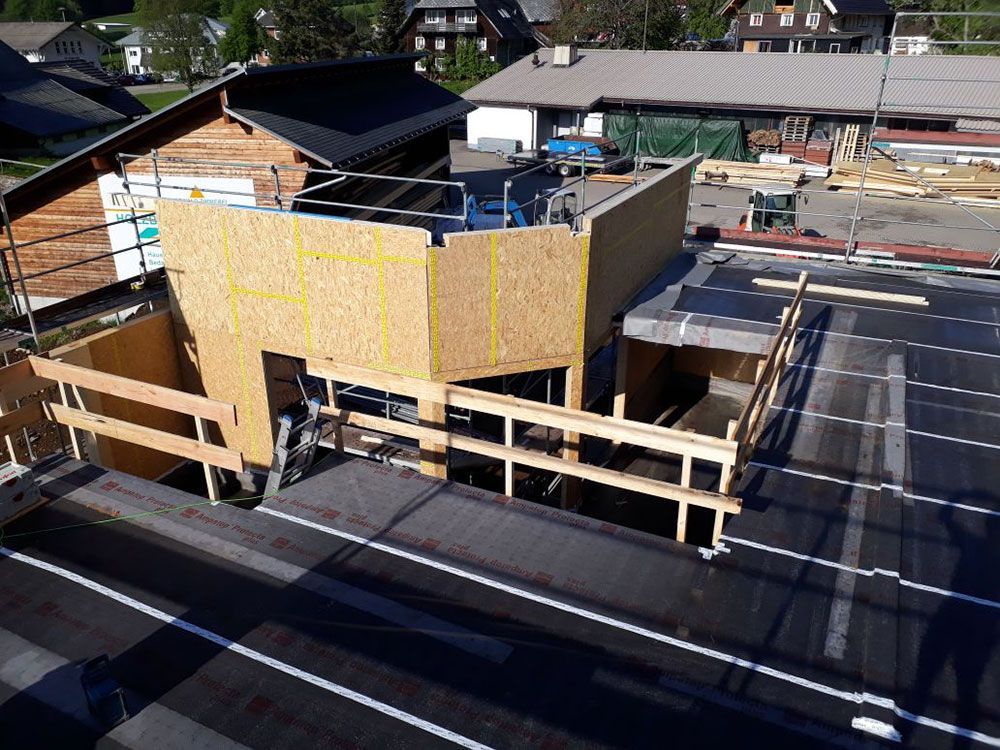 Baustelle mit OSB-Holzrahmenkonstruktion auf einem flachen, bitumenbedeckten Dach mit hölzernen Sicherheitsgeländern.